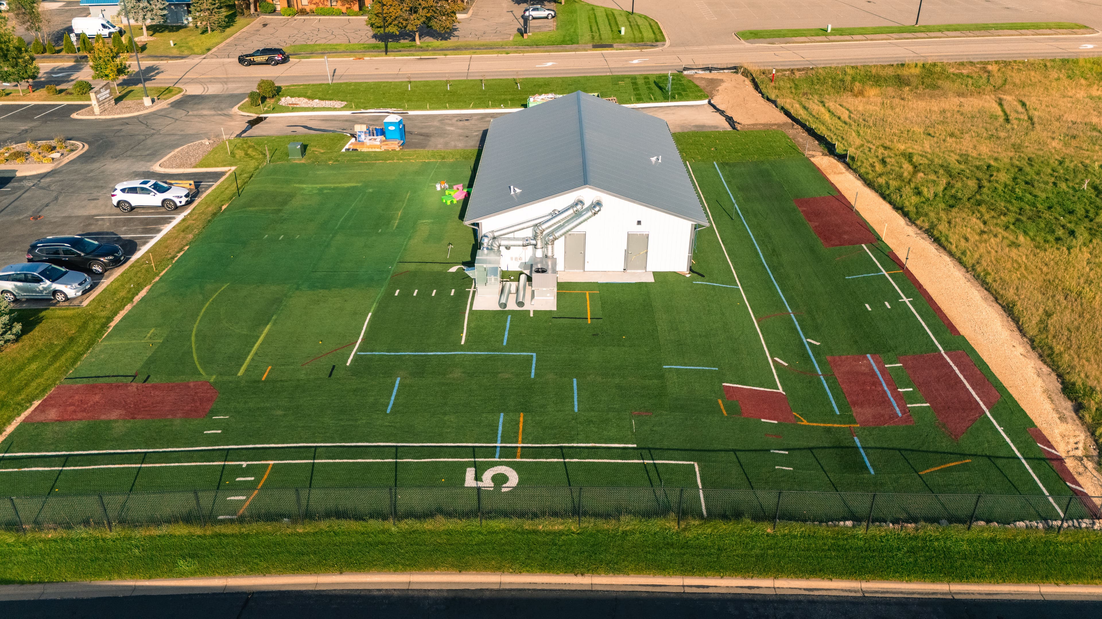 Aerial view of a modern sports facility with artificial turf and parking area.