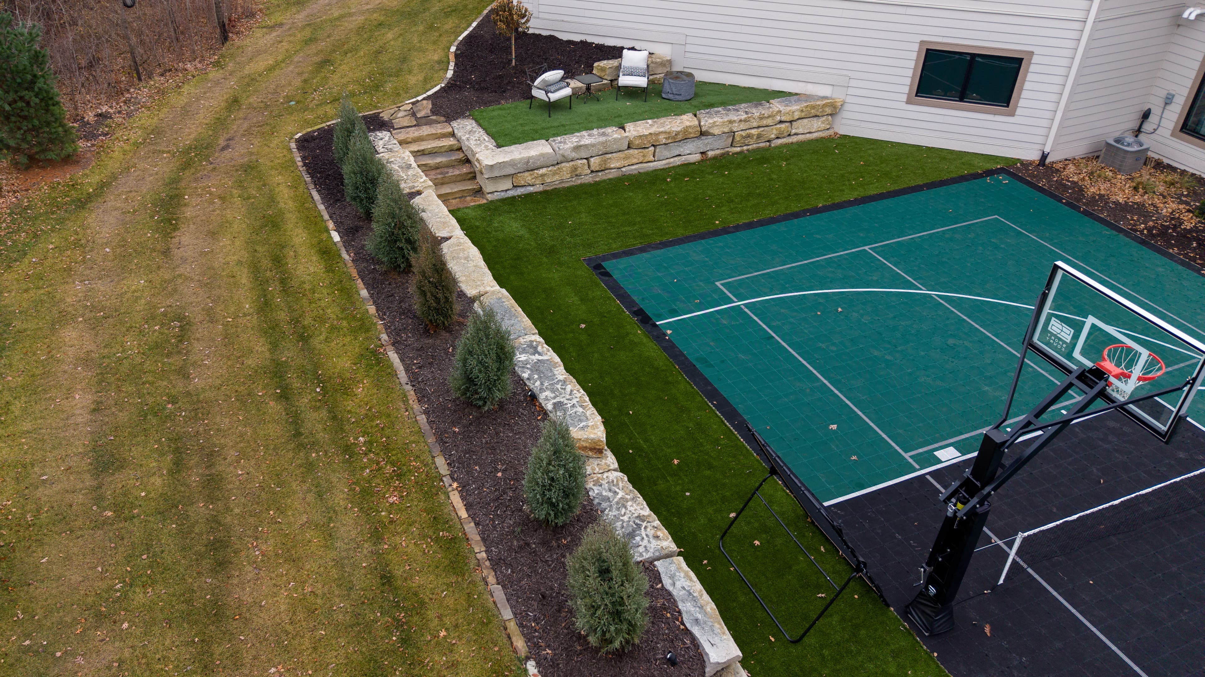 Aerial view of a backyard featuring a green basketball court, seating area, and landscaped path.