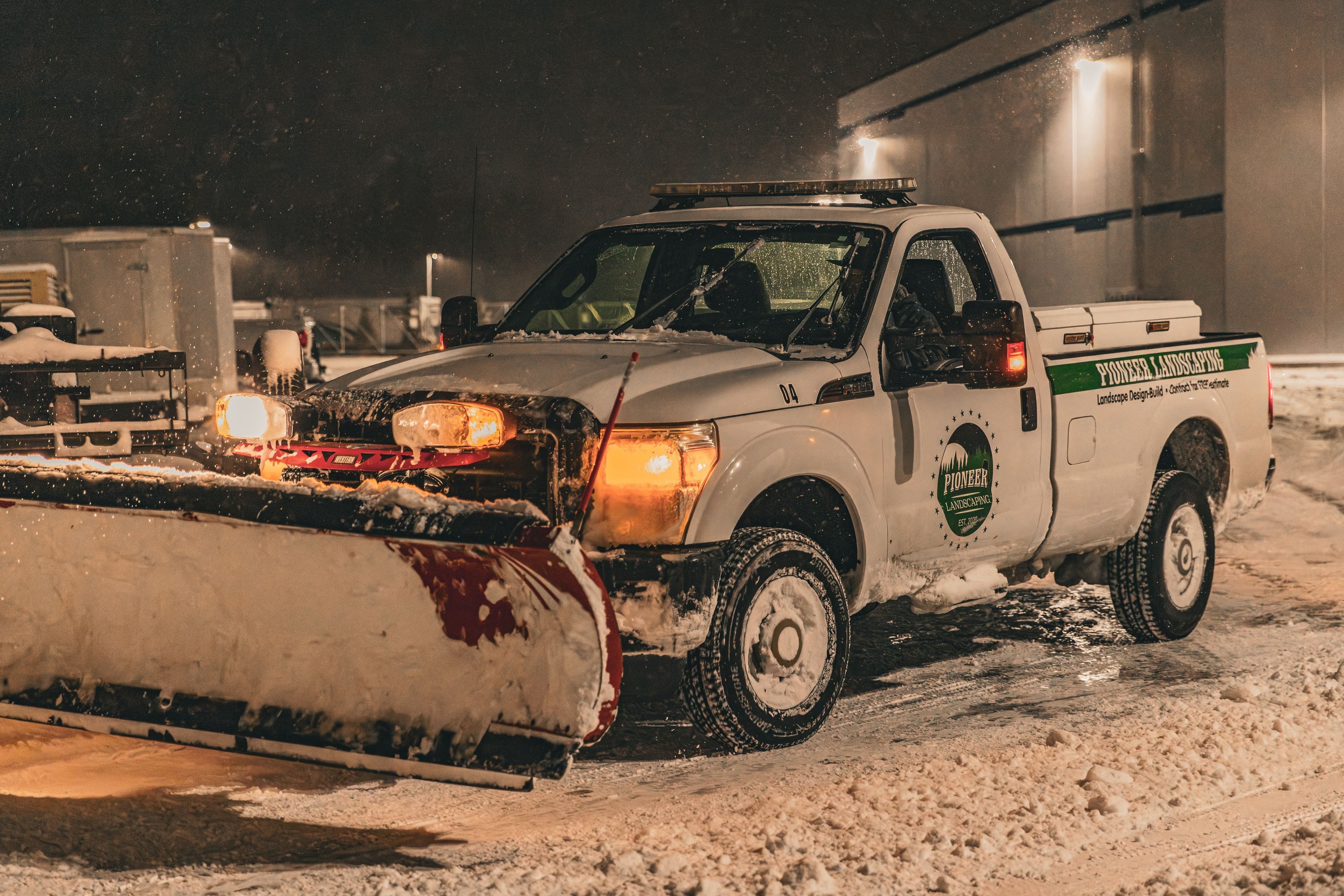 Snow plow truck clearing winter road at night in snowy conditions.