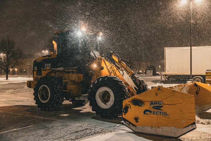 Snowplow clearing snow at night in a parking lot during a winter storm.