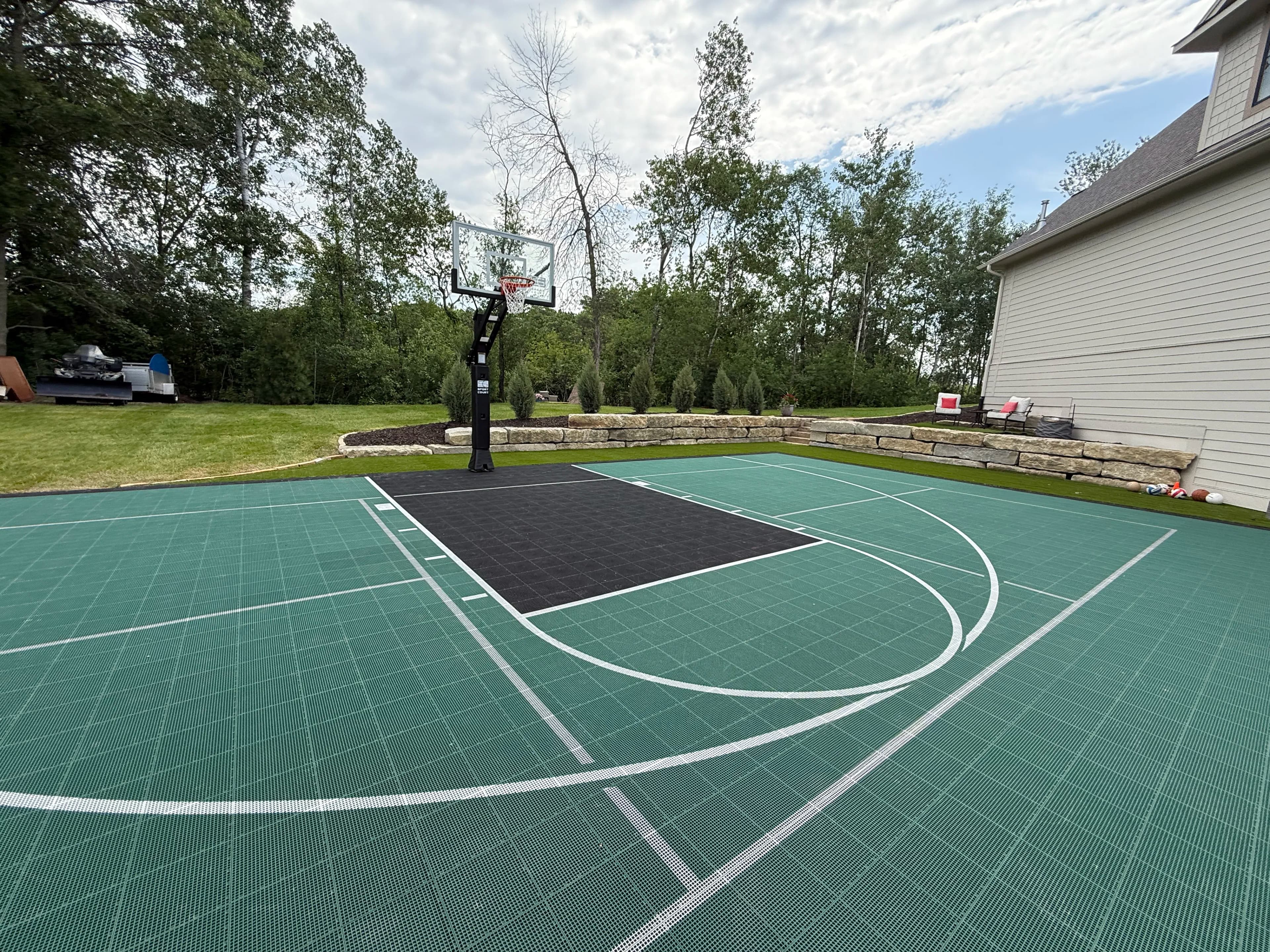 Outdoor basketball court with hoop, green flooring, and surrounding greenery.