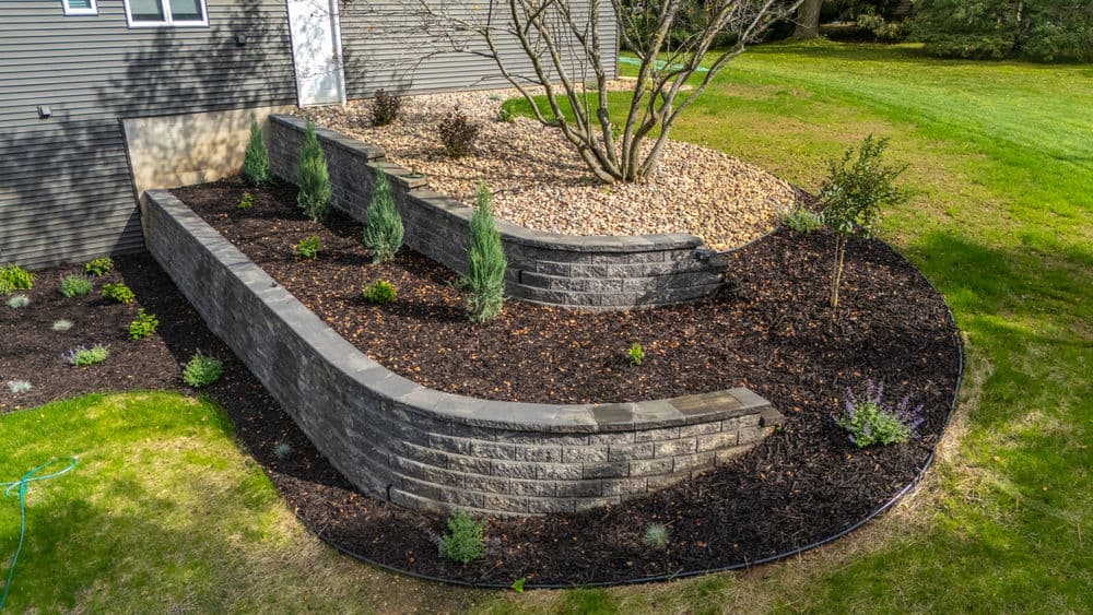Curved stone retaining wall with garden beds and ornamental plants in a residential landscape.